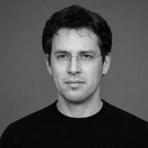 a man in his 30s with dark curly hair and glasses in the Black & White style